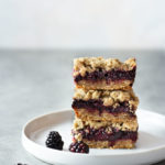 Straight on view of a stack of 3 Blackberry Crumble Bars on a white plate with a light background.