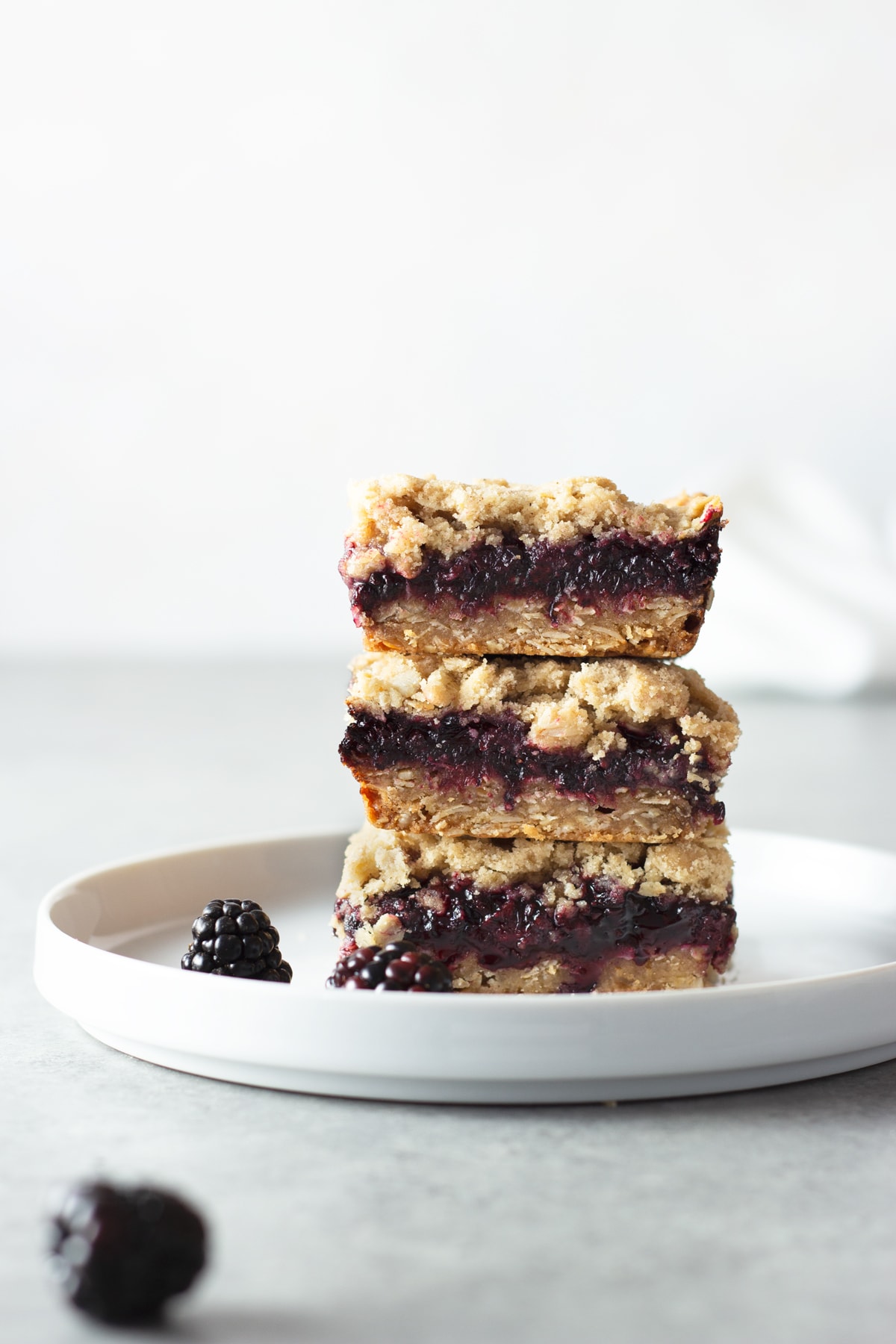 Straight on view of a stack of 3 Blackberry Crumble Bars on a white plate with a light background.