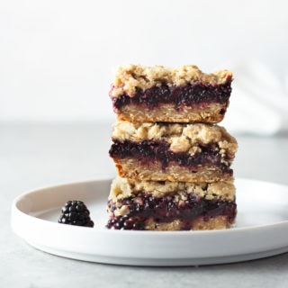 Straight on view of a stack of 3 Blackberry Oatmeal Crumb Bars on a white plate with a light background.