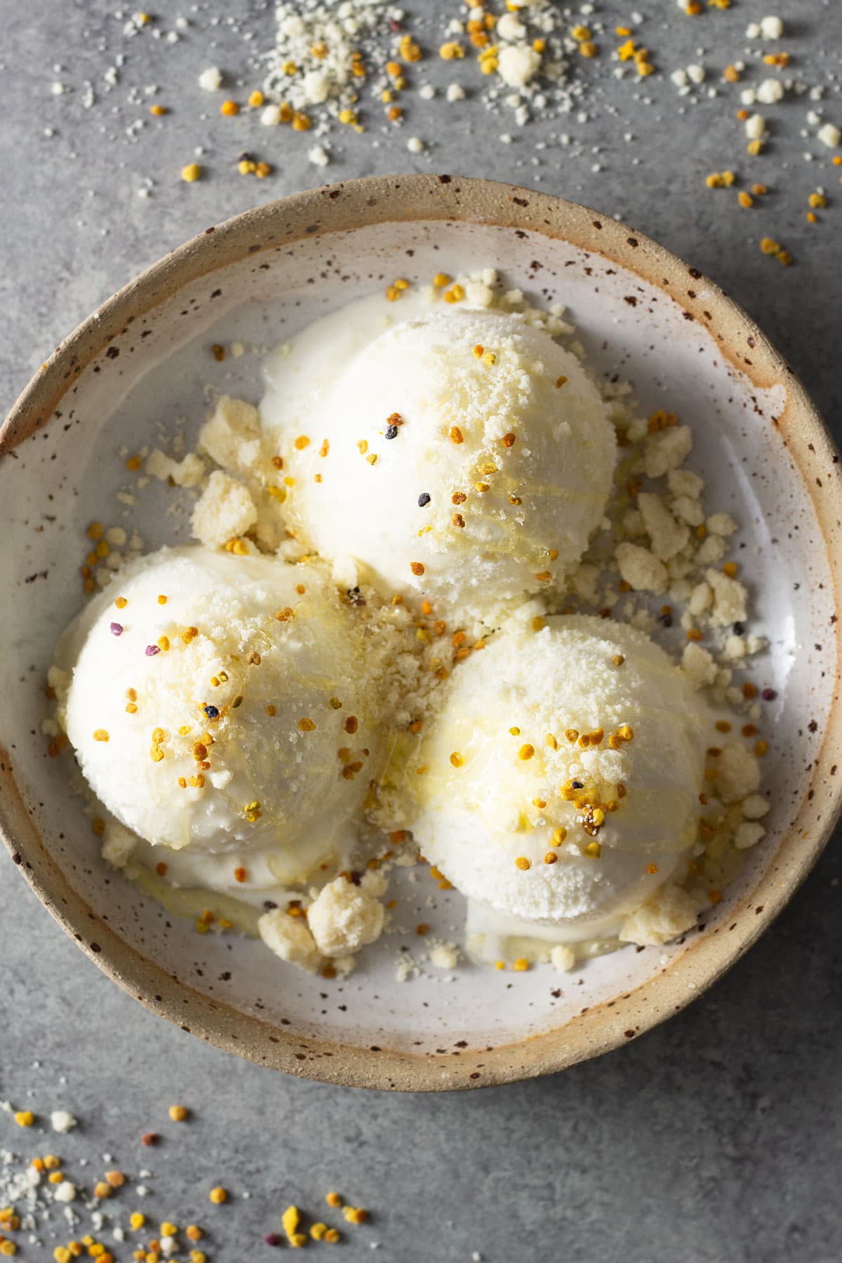 Overhead view of a rustic bowl with three scoops of milk and honey ice cream topped with honey, bee pollen and milk crumble.