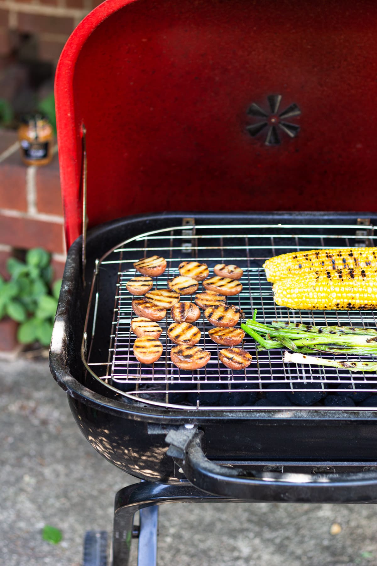 Red potatoes, corn on the cob and scallions on an outdoor grill.