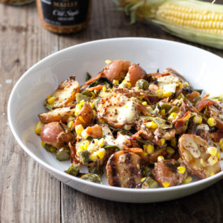 A bowl of Grilled Potato Salad with corn, bacon, and scallions on a wood surface.