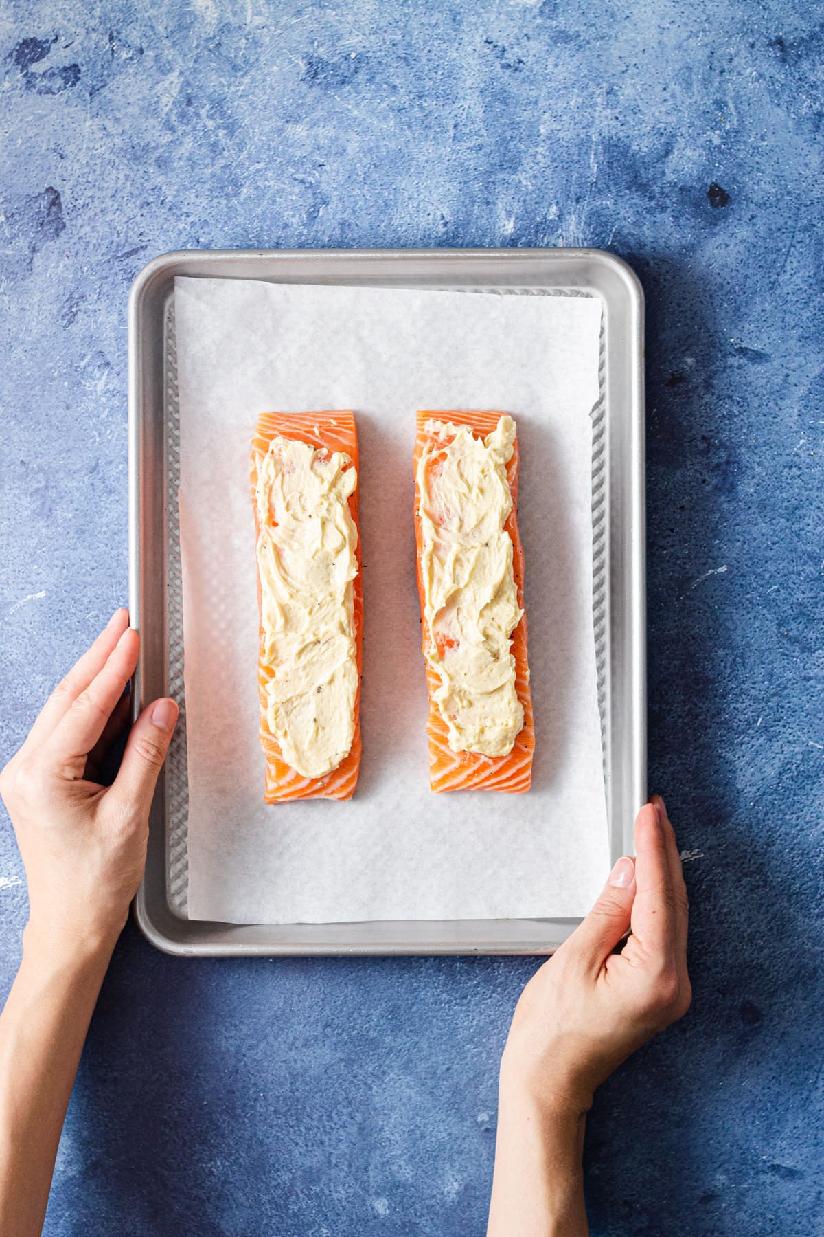 Overhead view of a sheet tray with raw salmon rubbed with miso butter on a blue background.