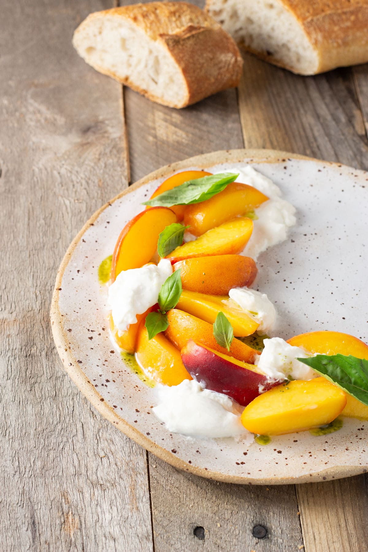 Angeled view of a rustic plate topped with sliced peaches, mounds of burrata cheese and fresh basil leaves.