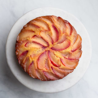 Overhead view of a Polenta Plum Upside Down Cake on a marble cake stand on a marble surface.