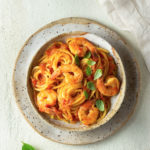 Overhead view of a rustic bowl of shrimp spaghetti on a textured, light colored surface.