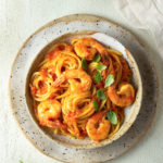 Overhead view of a rustic bowl of shrimp spaghetti on a textured, light colored surface.