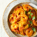 Overhead closeup view of a bowl of shrimp spaghetti with tomato sauce and small basil leaves on top.