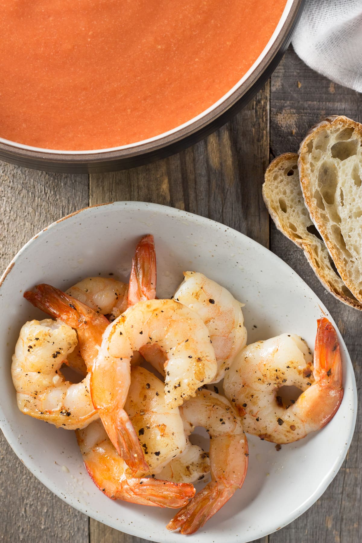 Sautéed shrimp in a bowl next to bread and tomato soup.
