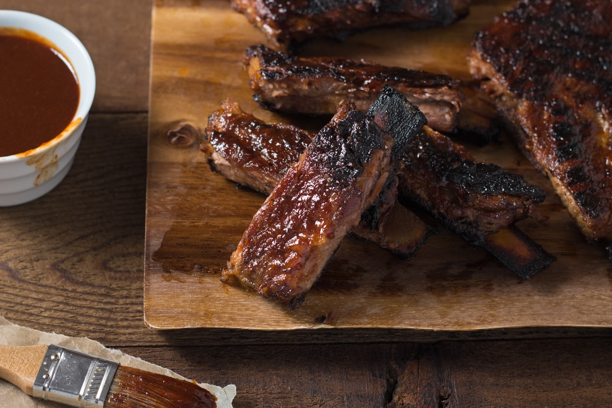 Korean BBQ Pork Ribs on a wood cutting board next to a bowl of barbecue sauce.
