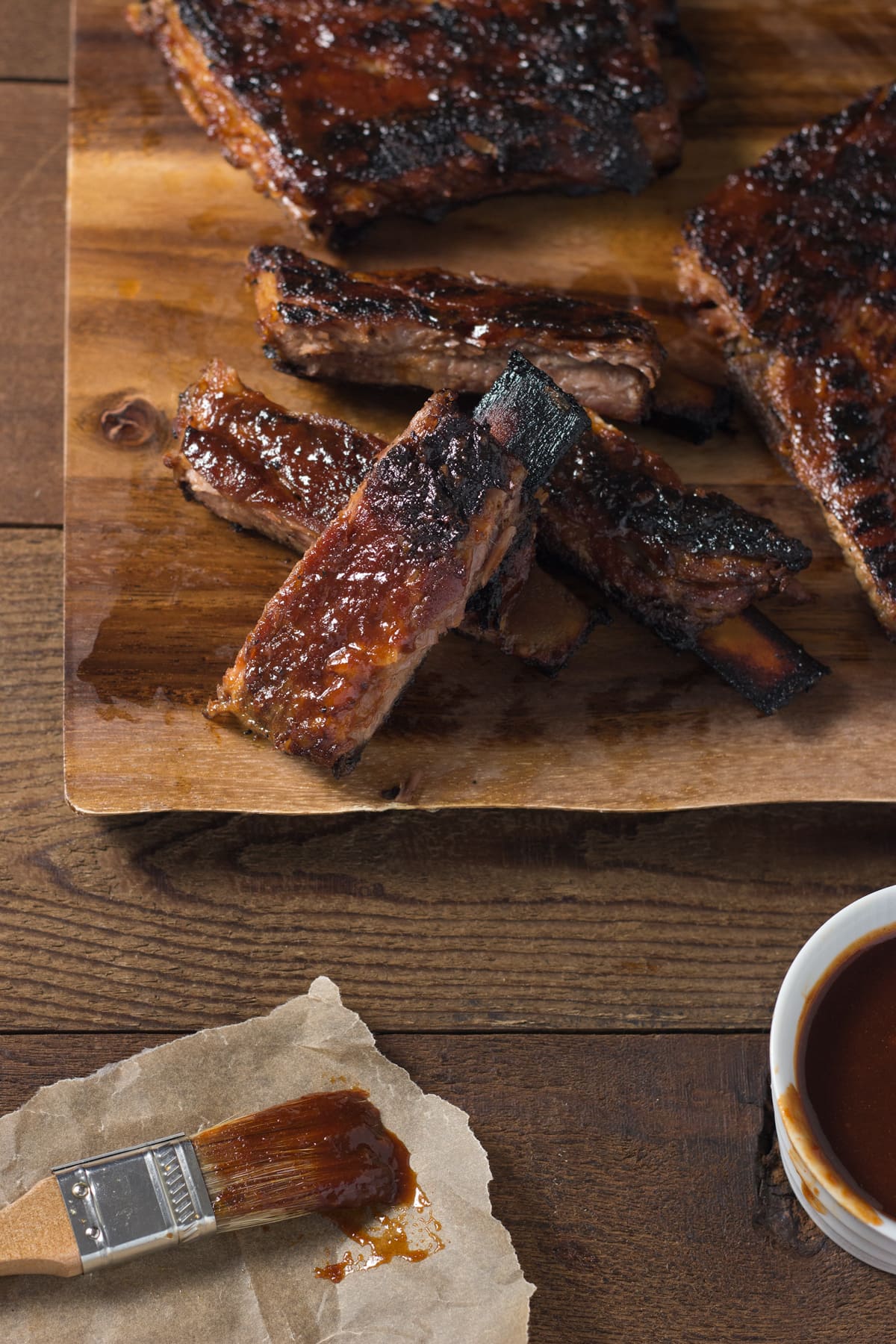Group of Korean BBQ pork ribs on a cutting board next to a bowl of barbecue sauce and a pastry brush.
