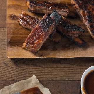 Group of Korean BBQ pork ribs on a cutting board next to a bowl of barbecue sauce and a pastry brush.