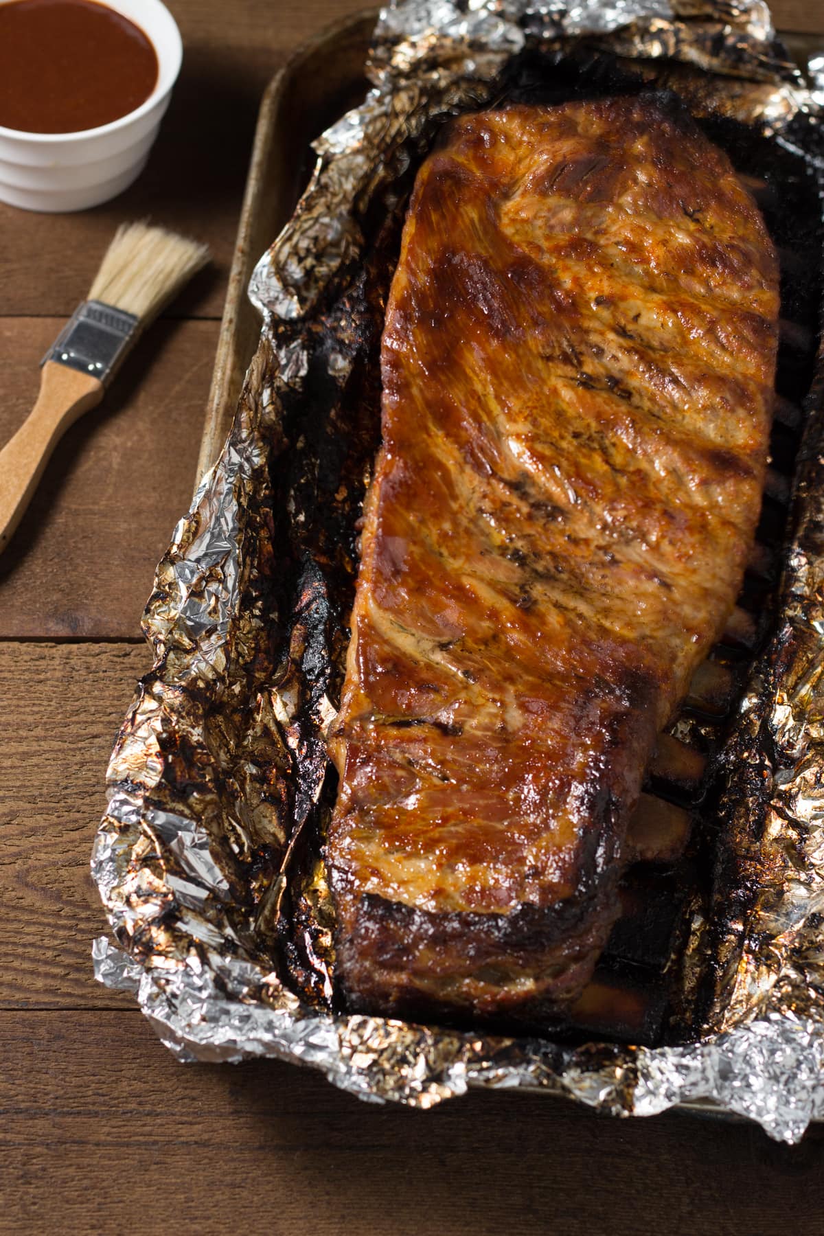Rack of pork spare ribs in foil on a sheet tray brushed with barbecue sauce.