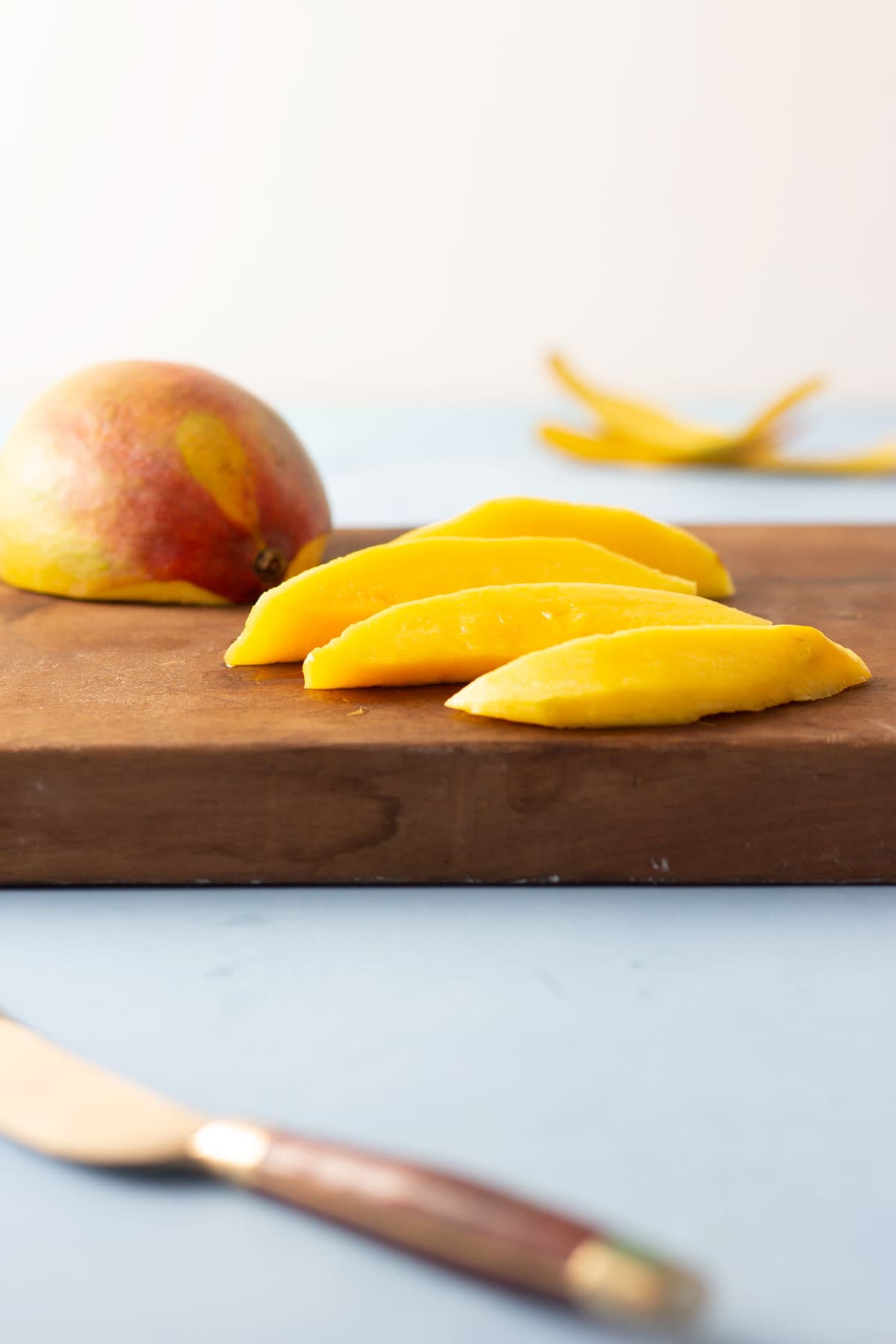 Fresh mango slices and half a mango on a cutting board with a knife in the forefront.