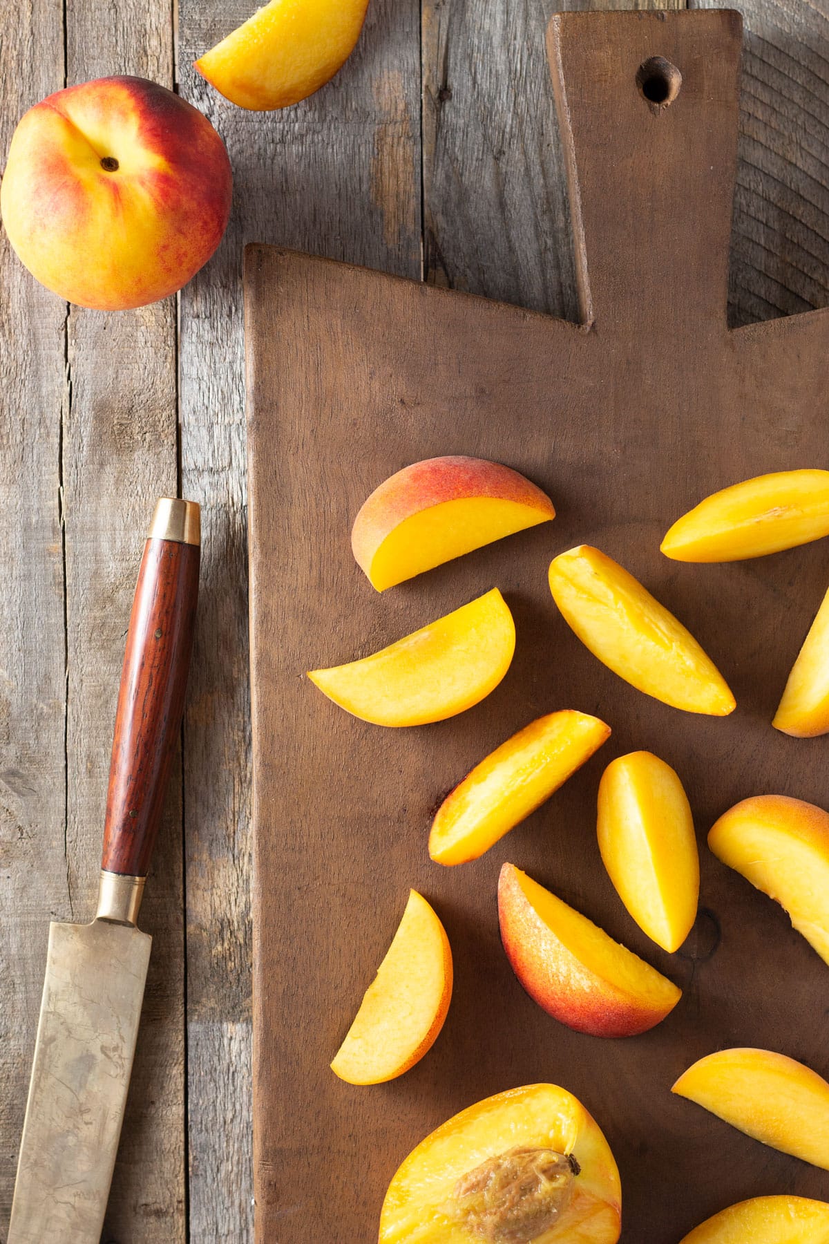 Sliced Peaches on a wood cutting board next to a whole peach and a knife.