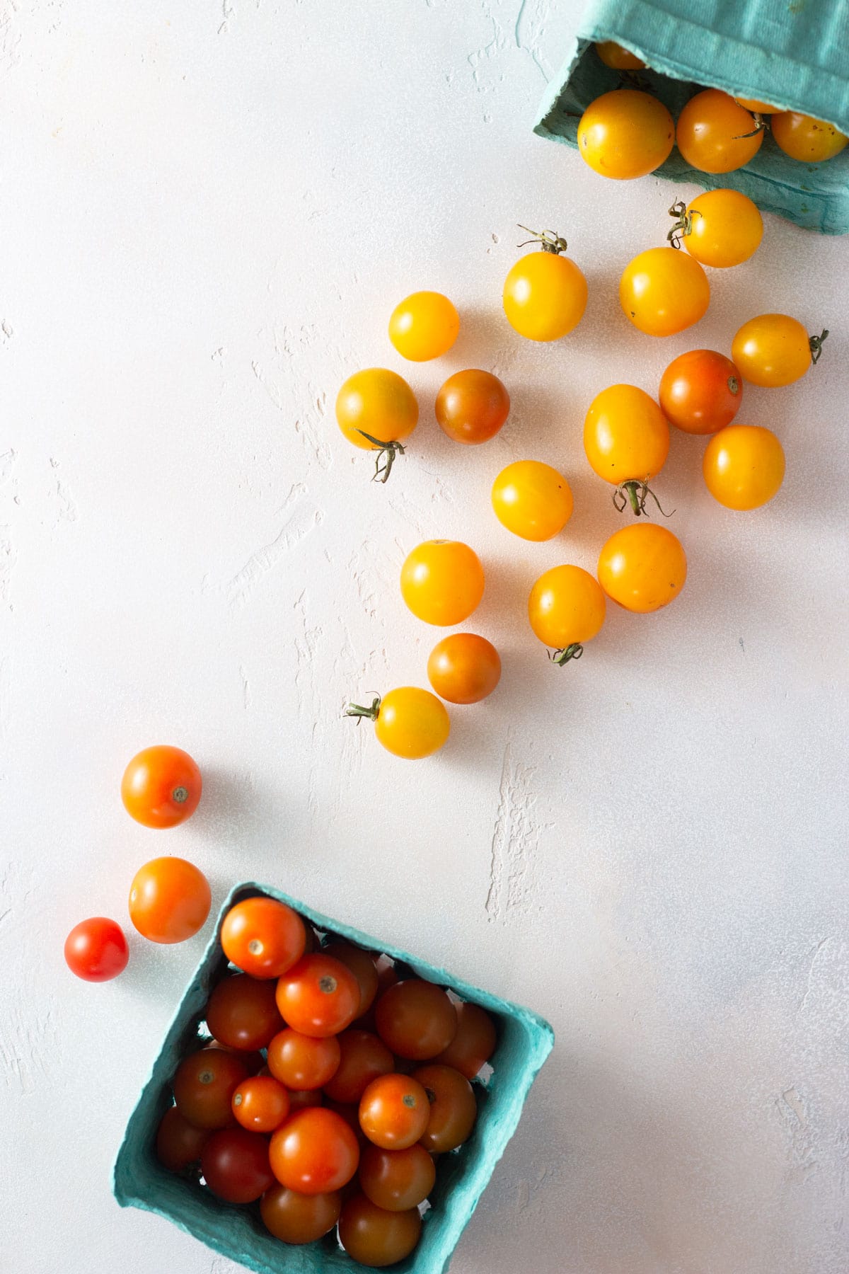 Overhead view of red and yellow grape tomatoes on a light surface.