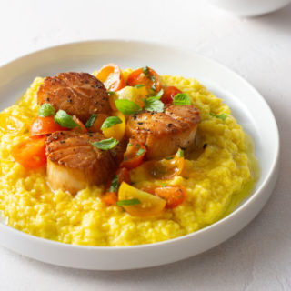 Angled view of a plate of Seared Scallops with Fresh Corn Polenta and Tomato Salad.