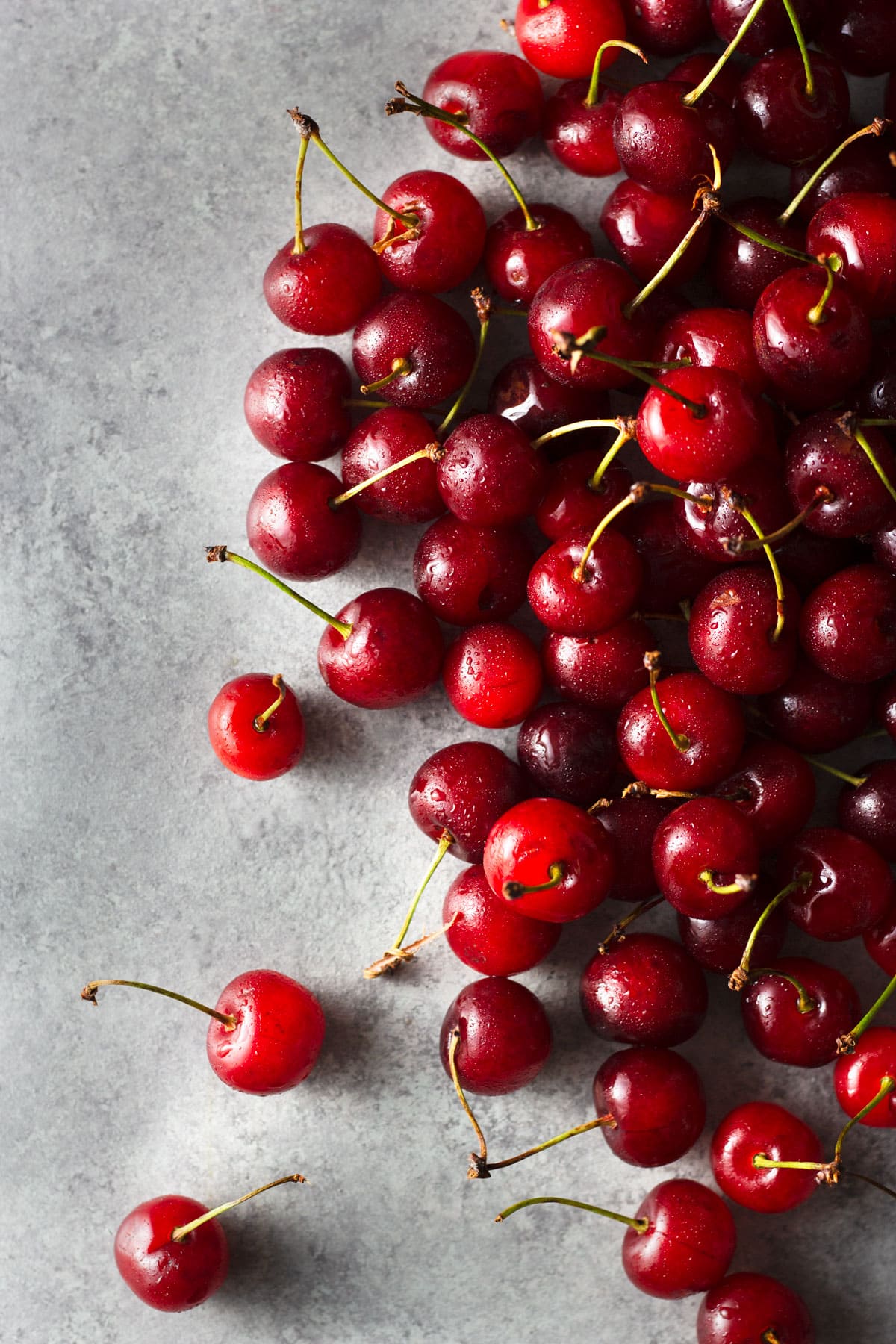 Overhead view of a group of sour cherries on a light grey surface.
