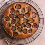 Fig and Almond Cake on a cooling rack next too a cake server and serving dishes.