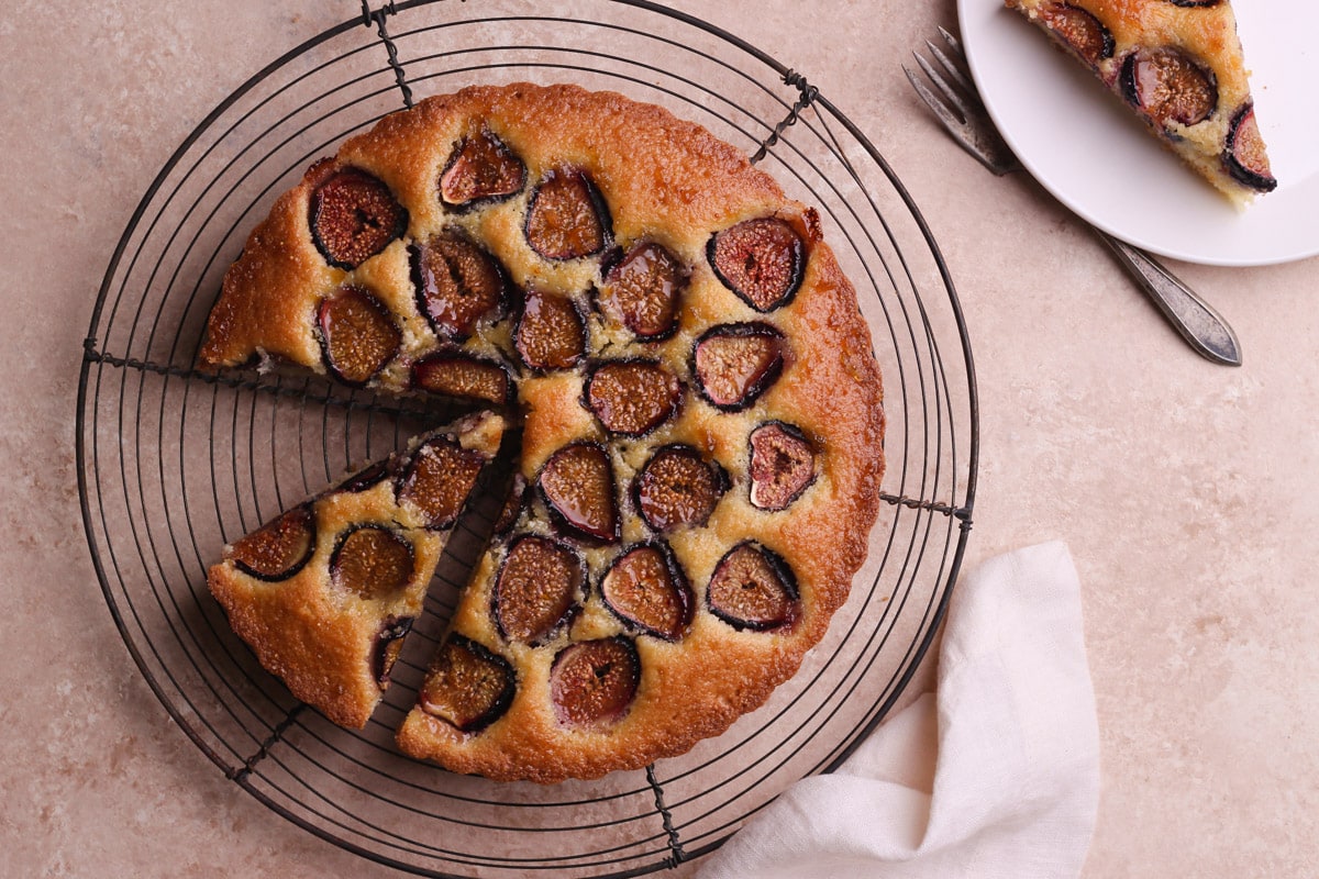 Overhead view of a fig cake with slices cut out and a slice on a plate in the upper right corner.
