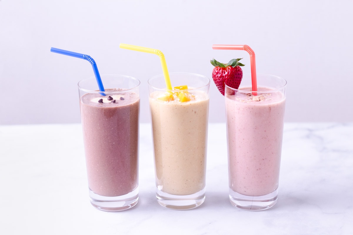 Three breakfast oatmeal smoothies lined up: chocolate, mango and strawberry.
