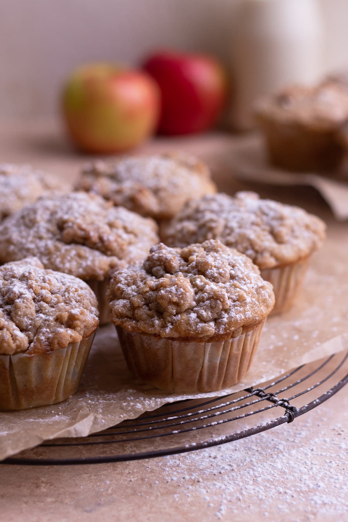 Spiced Apple Sour Cream Muffins with Crumb Topping on a cooling rack with more muffins, milk and apples in the background.