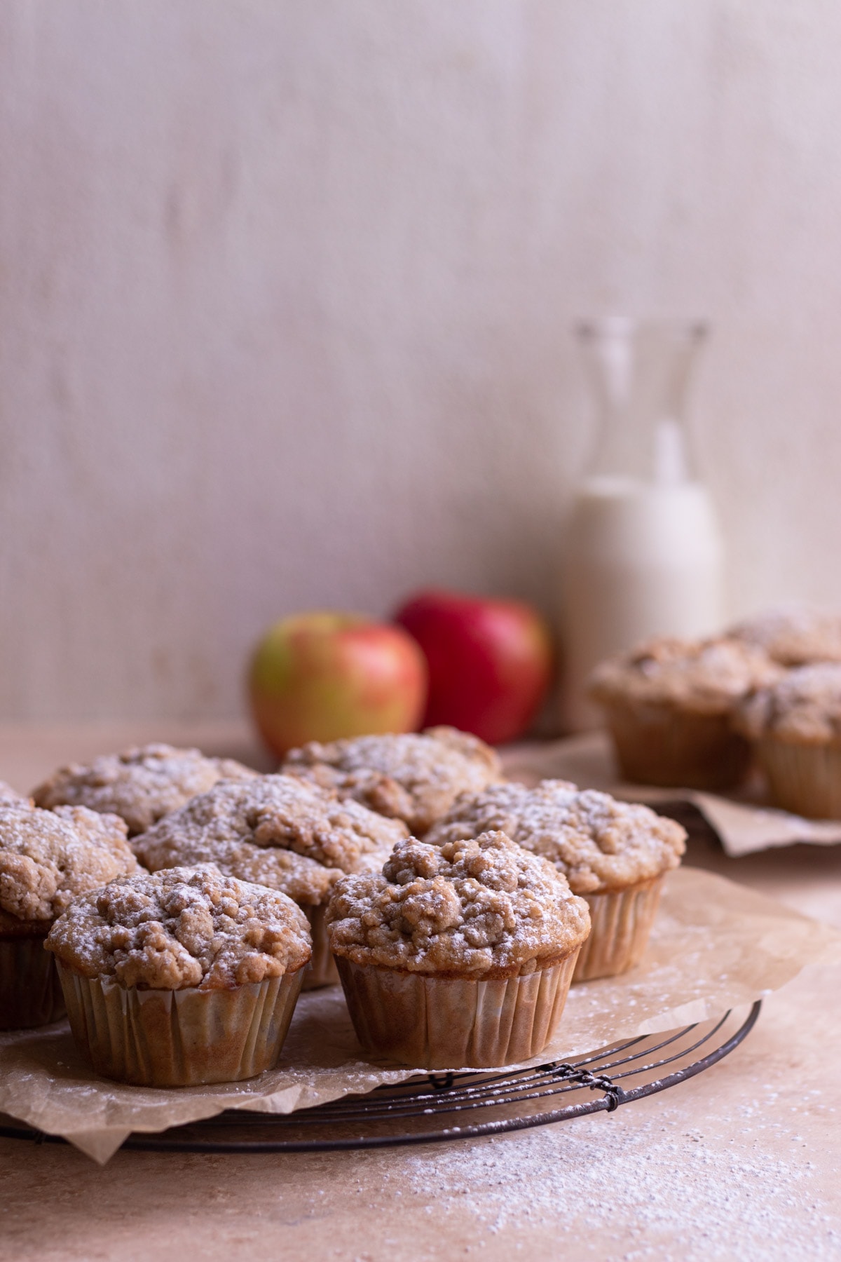 Crumble Muffins on parchment on a wire rack with more muffins, milk and apples in the background.