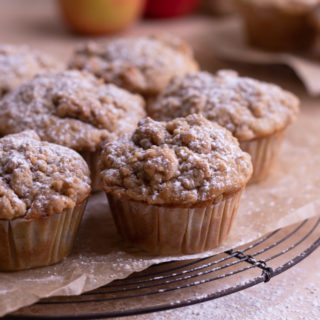 Close up of a group of Apple Crumb Muffins on a cooling rack with apples in the background.