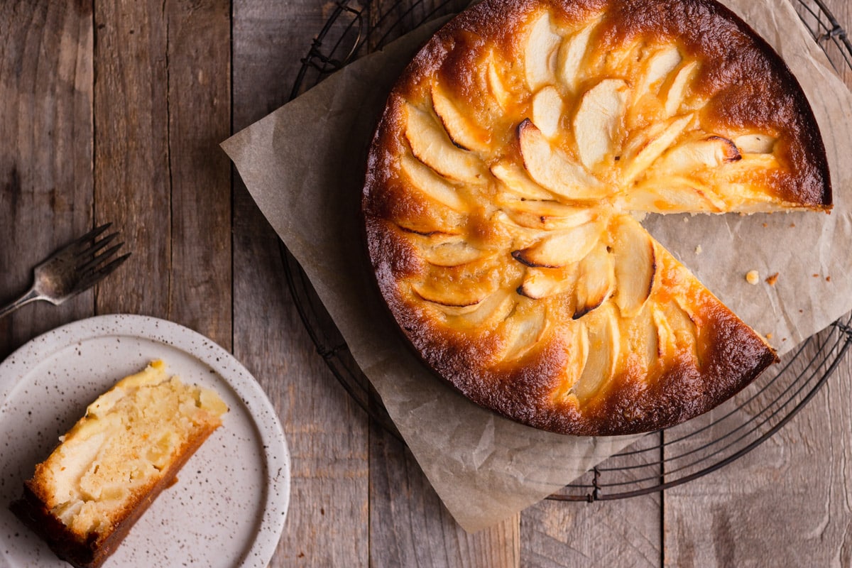 Apple Almond Cake with a slice cut out on a plate on a rustic wood surface.