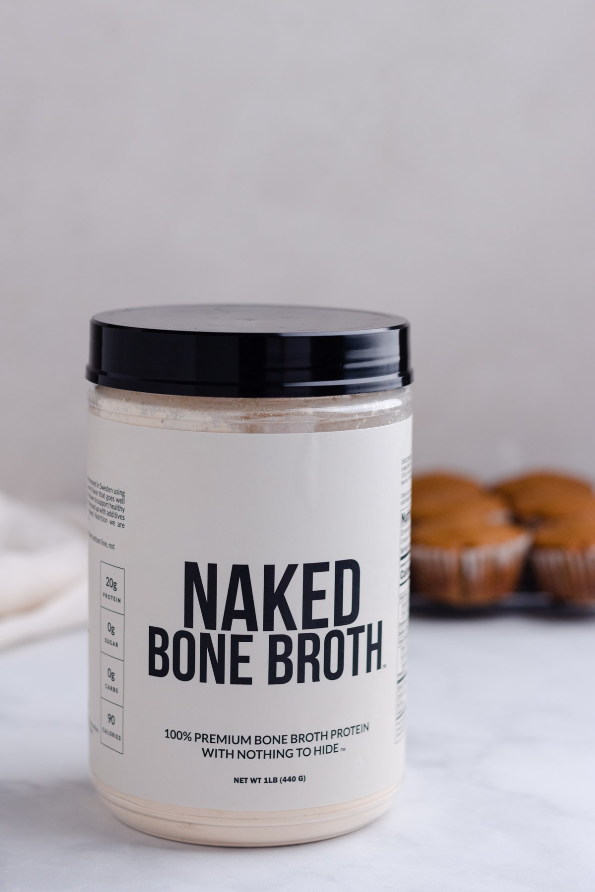 A close up of Naked Bone Broth protein powder with muffins in the background.