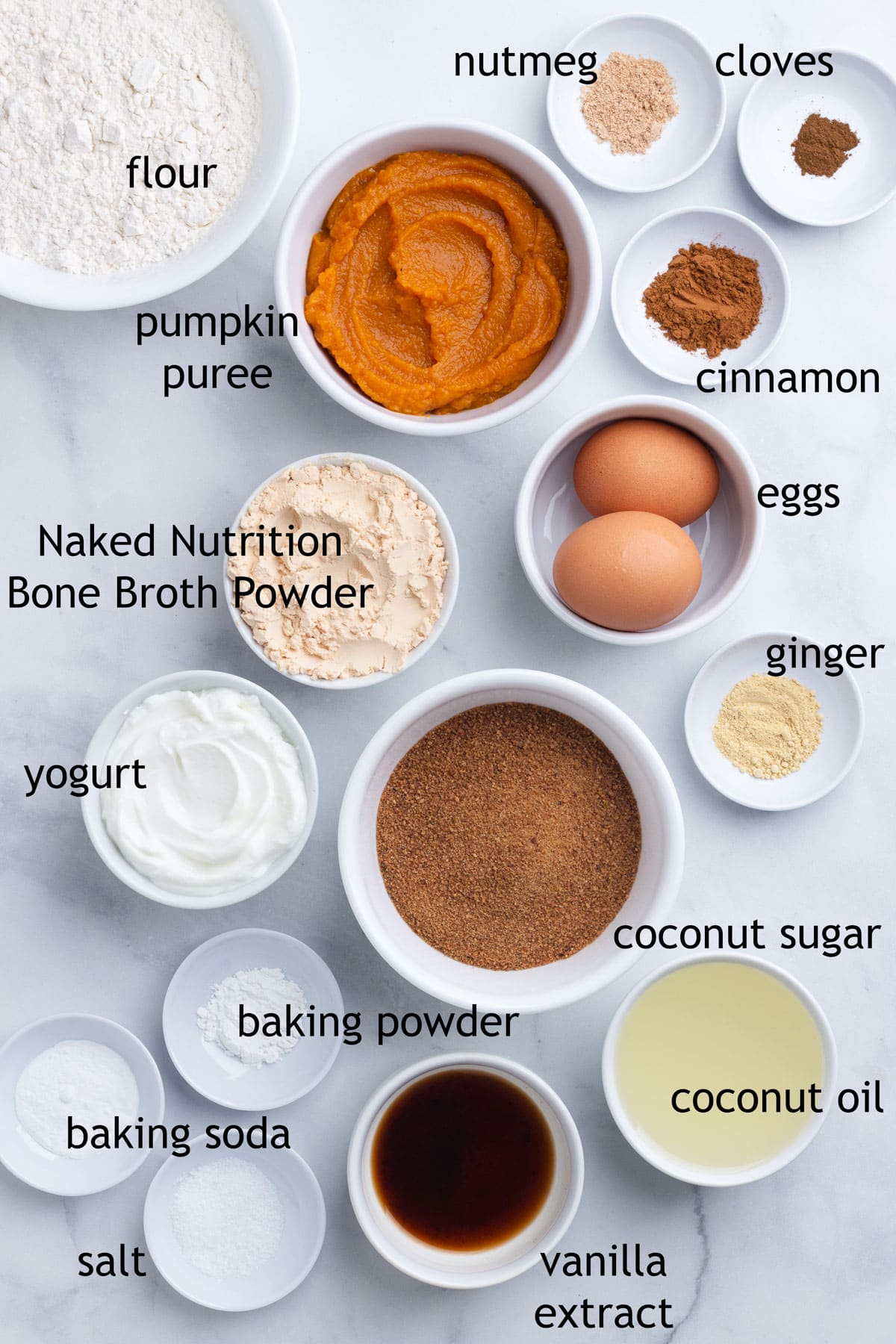 Ingredients for muffins including flour, pumpkin puree, spices, protein powder, eggs, coconut sugar, coconut oil and yogurt.