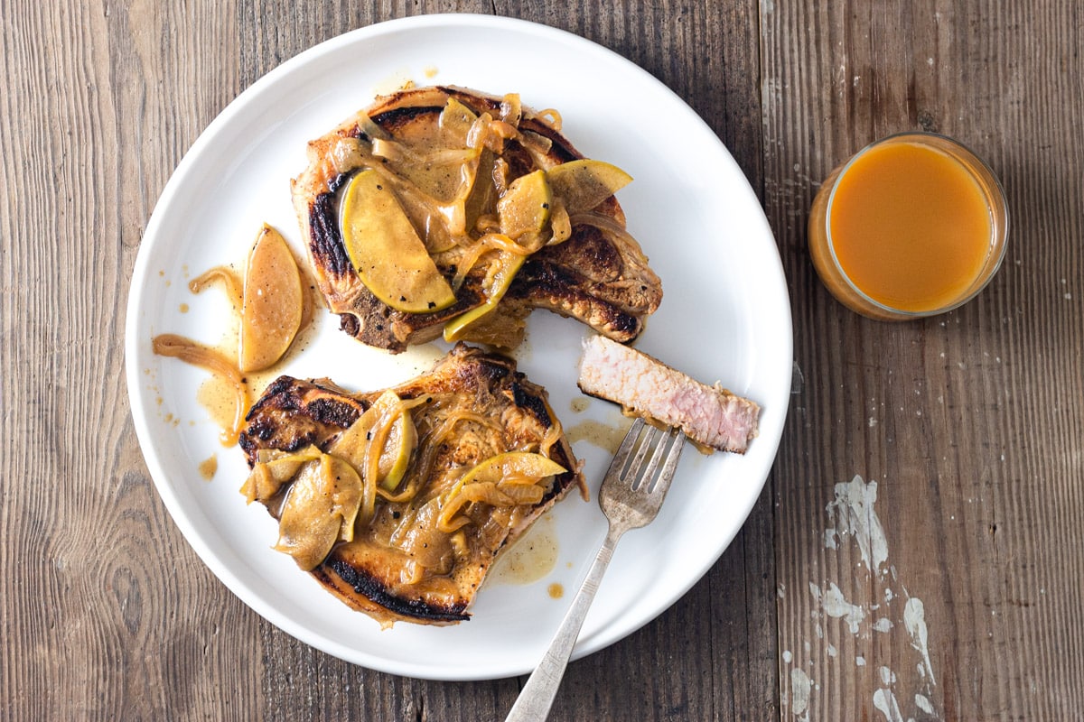 Pork chops with Caramelized Apples and Onions on a plate on a wood surface with a slice cut out.