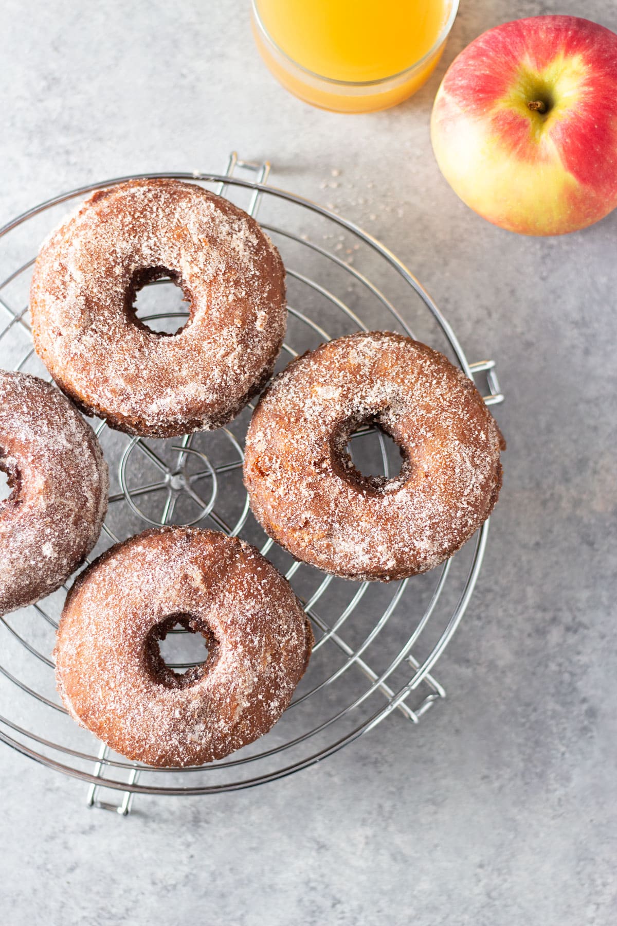 Old Fashioned Apple Cider Donuts on a wire rack next to an apple and glass of apple cider.