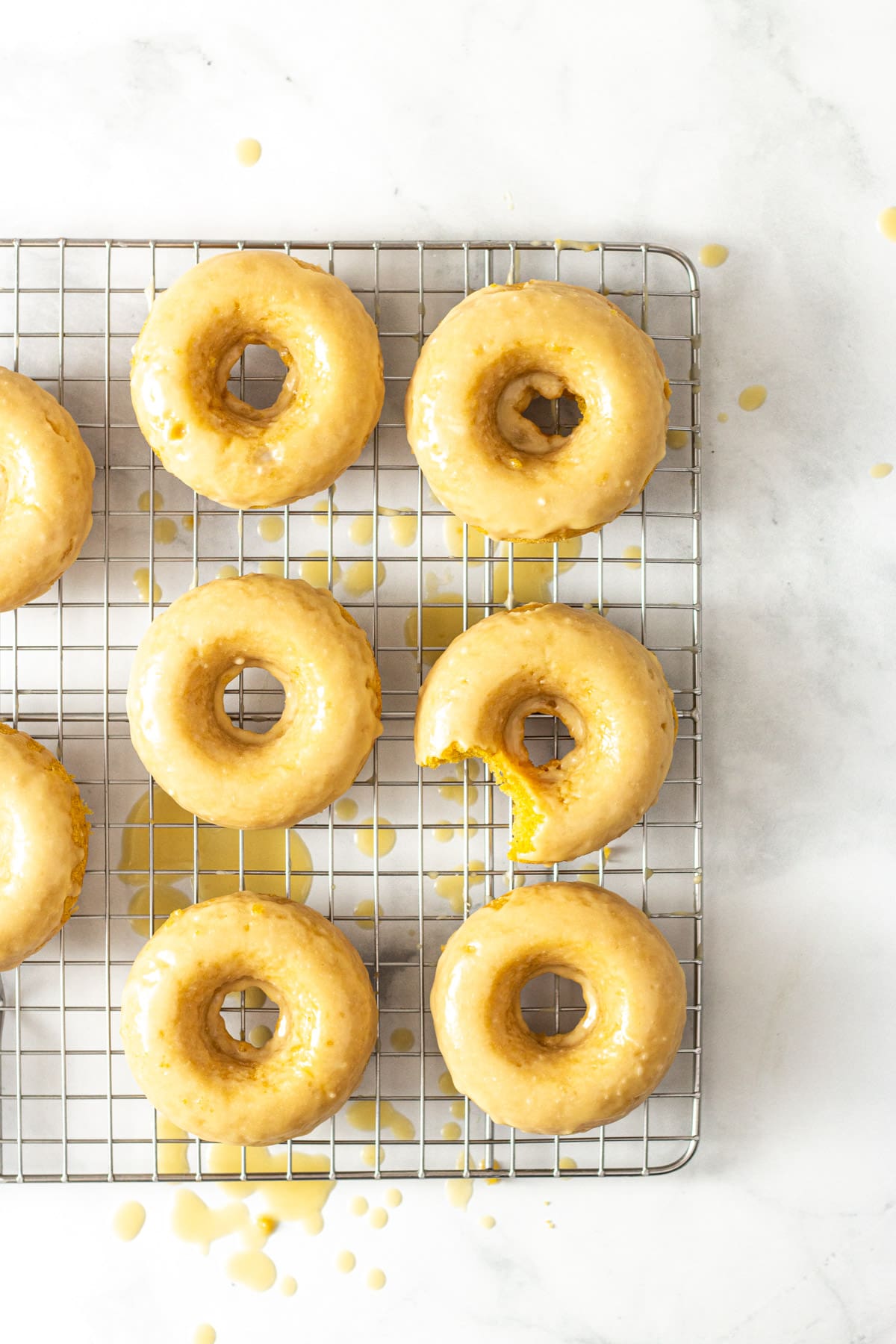 Overhead image of Baked Pumpkin Donuts with Maple Glaze on a wire rack on a marble surface.