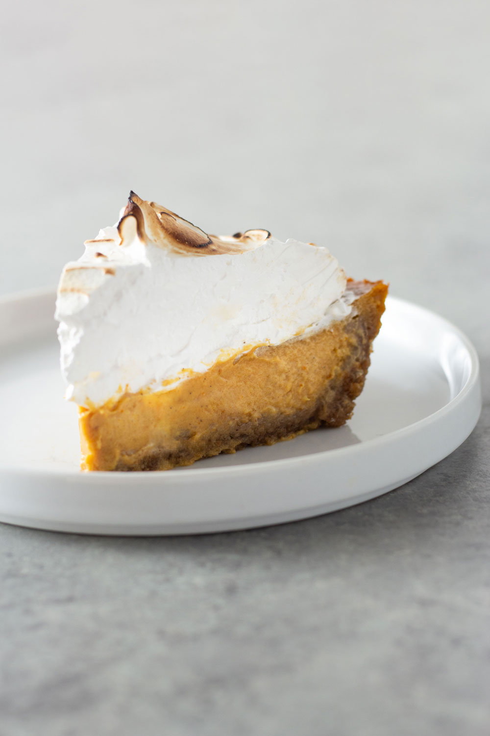 Straight on view of a slice pumpkin meringue pie on a grey, textured surface.