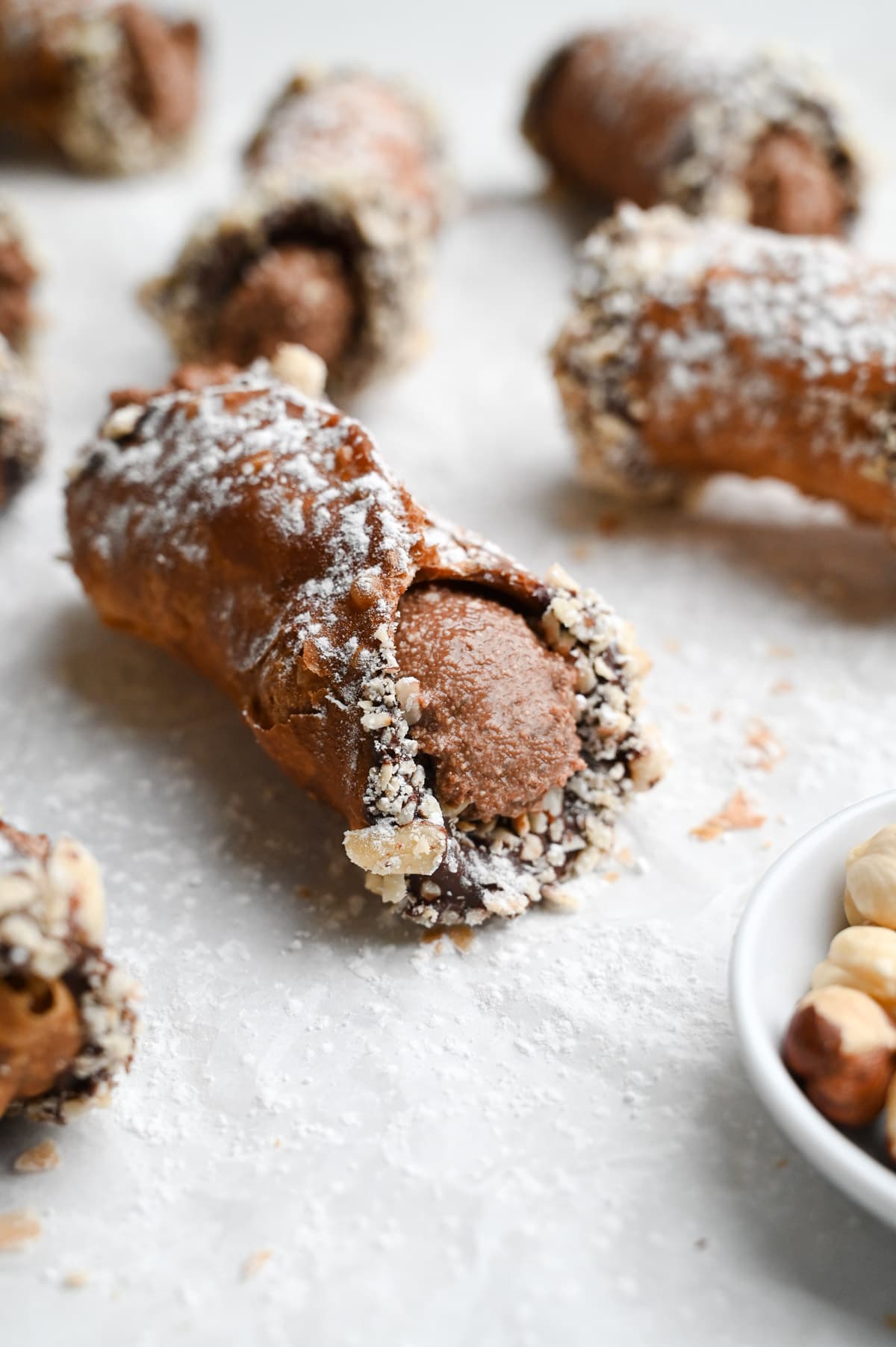 Close up of a group of Nutella cannoli dipped in chocolate and hazelnuts on parchment paper.