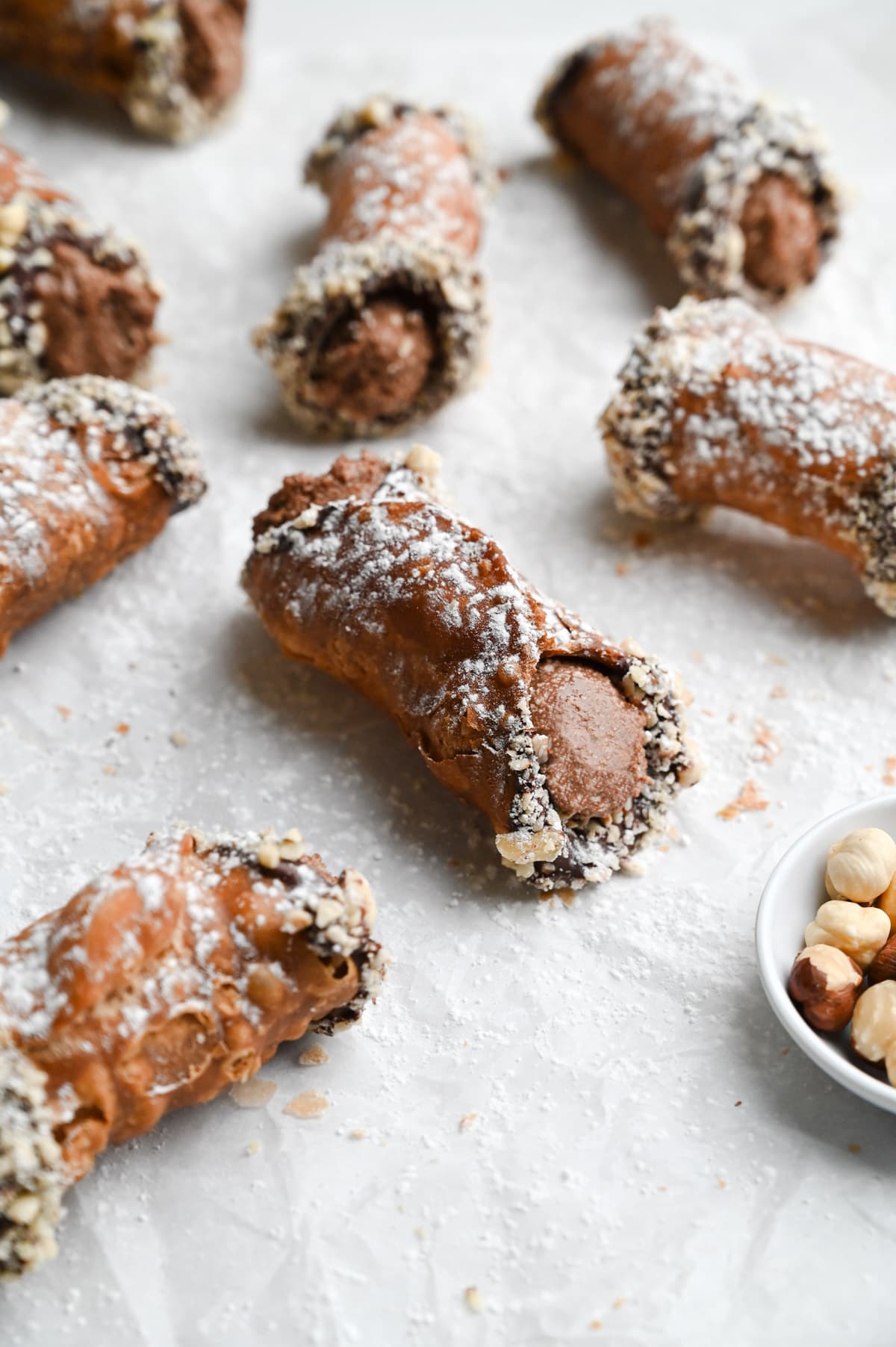 A group of Nutella cannoli dipped in chocolate and hazelnuts on parchment paper.