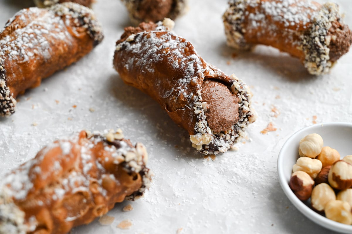 Close up of a group of Nutella cannoli dipped in chocolate and hazelnuts on parchment paper.