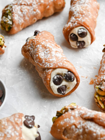Angled view of a group of cannoli decorated with pistachios and chocolate chips.