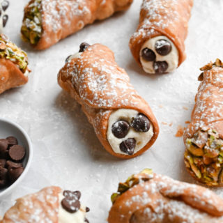 Angled view of a group of cannoli decorated with pistachios and chocolate chips.