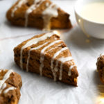 Close up of gingerbread scones on parchment with Christmas lights and a bowl of lemon glaze.