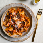 Short Rib Ragu with Pappardelle Pasta in a rustic bowl on a textured, cream surface.