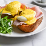 Close up, straight on view of a plate of Eggs Benedict with arugula.