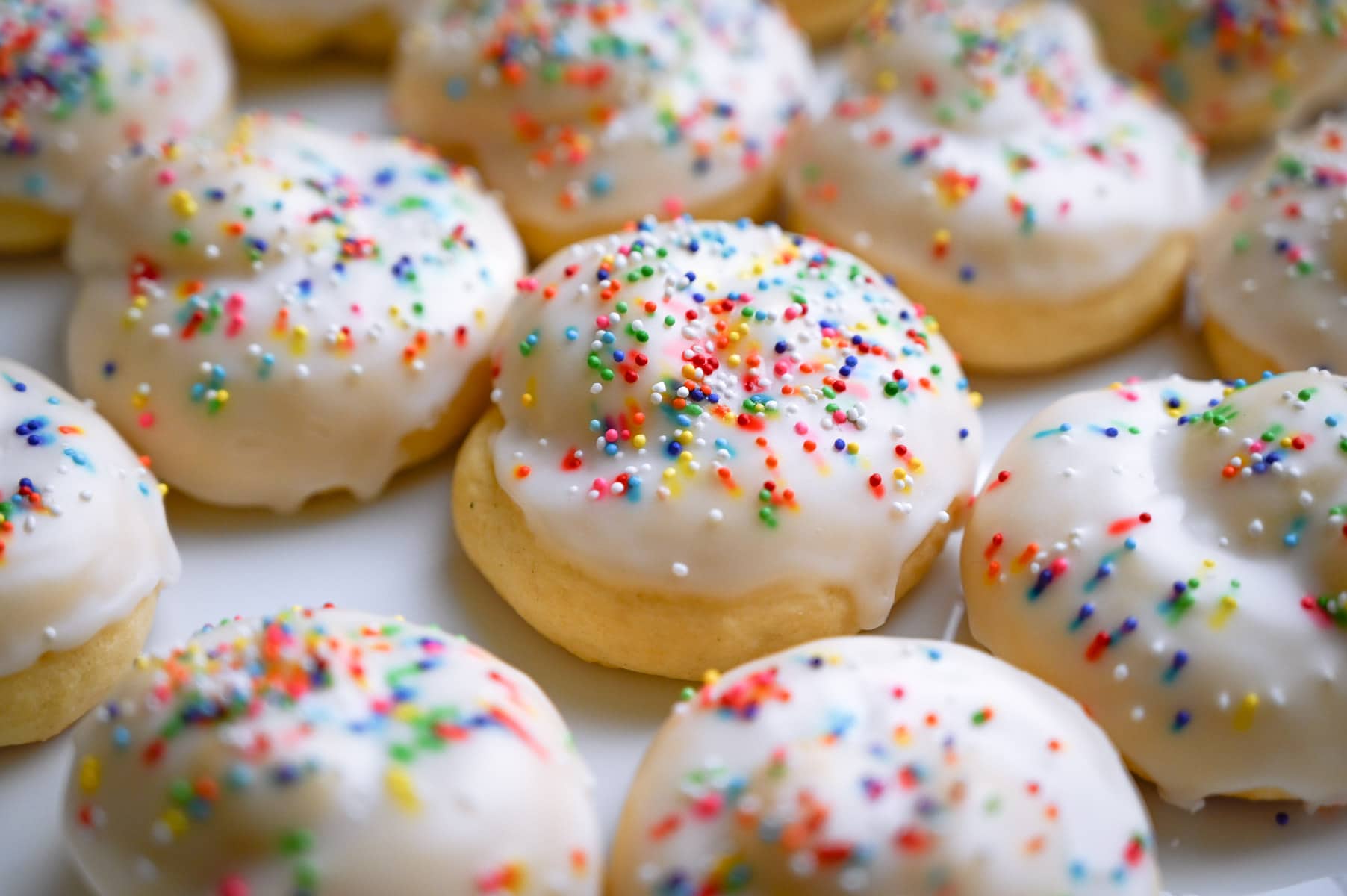 Close up of a group of Italian knot cookies with white glaze and colorful sprinkles.