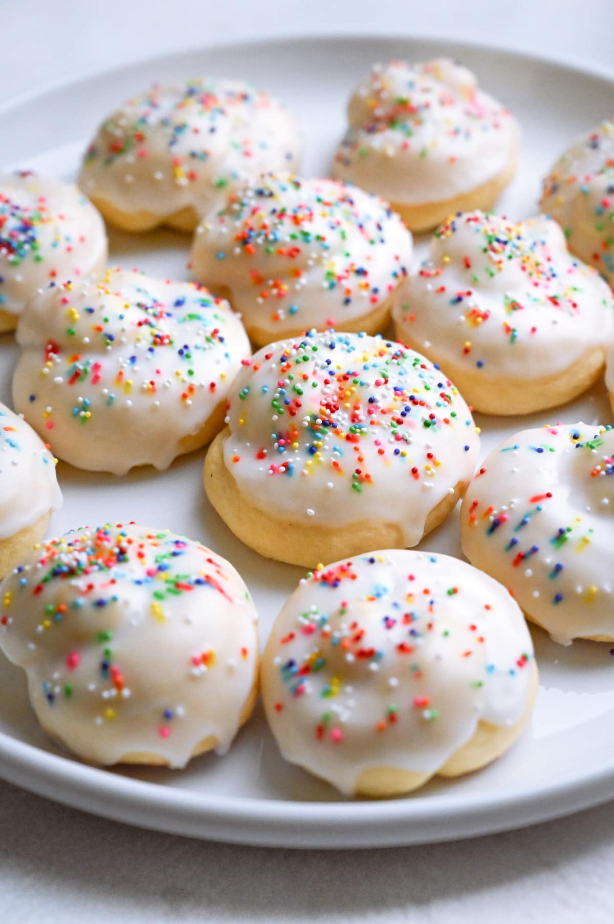 Plate of Knot Cookies topped with rainbow nonpareil sprinkles on a white plate.