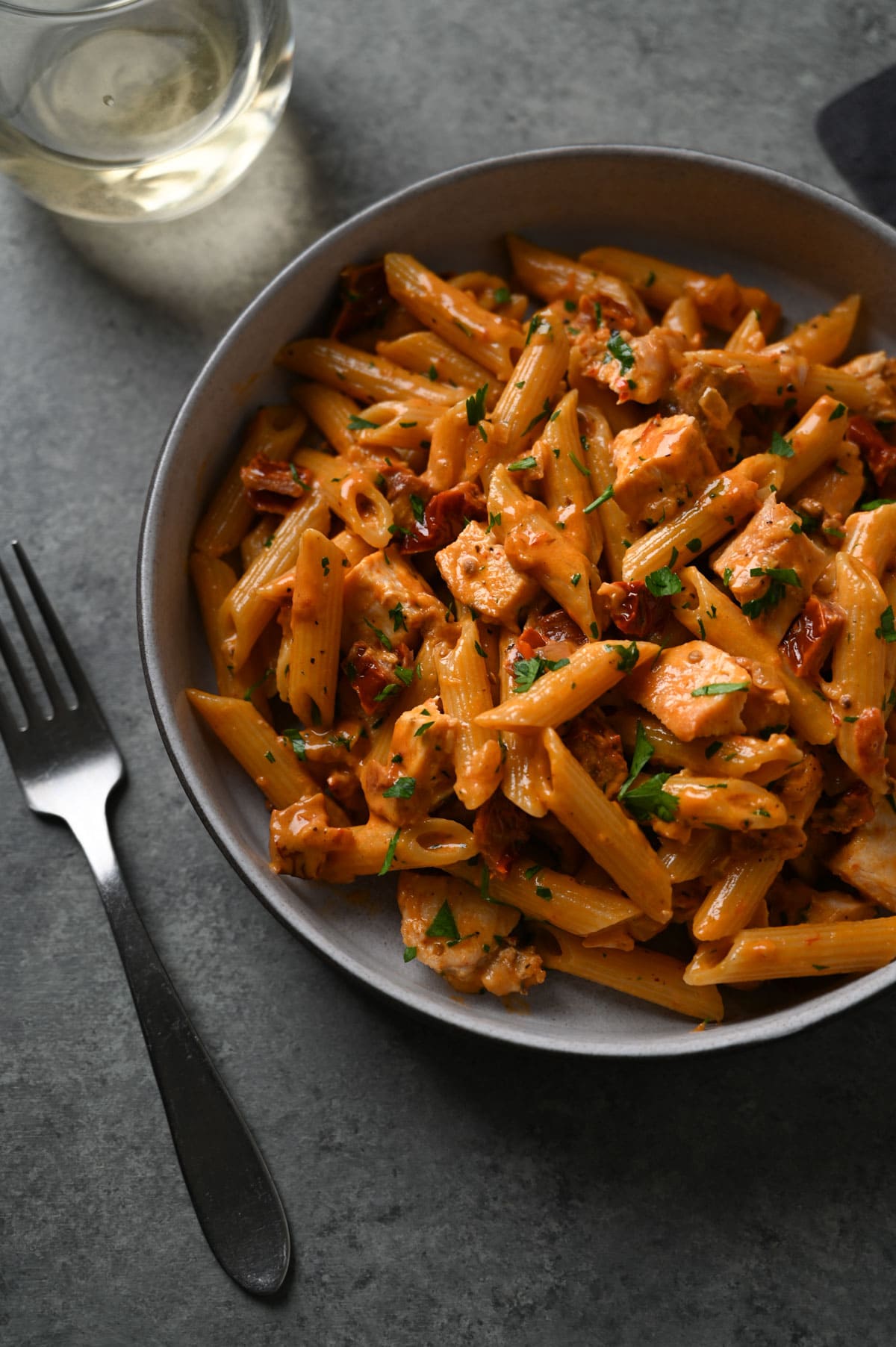 Angled, close up view of a bowl of pasta with chicken and tomato cream sauce. 
